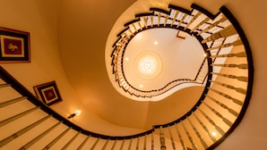 Un escalier en colimaçon, avec un luminaire central et des tableaux encadrés accrochés aux murs.