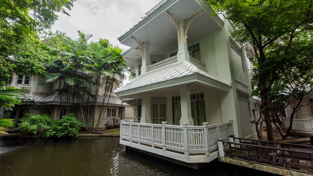 Un bâtiment à deux étages doté d’un balcon, entouré d’une végétation luxuriante et bordé par un plan d’eau.