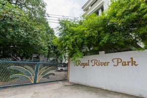 A gated entrance to Royal River Park with a white wall and a metal gate. - Royal River Park (Bangkok)