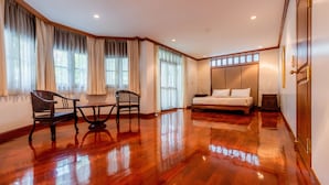 Une pièce spacieuse dotée d’un plancher en bois poli, d’un grand lit, d’un bureau avec une chaise et de grandes fenêtres avec des rideaux.