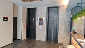 Zona de ascensores con dos elevadores, un mostrador de recepción y un cartel en la pared.