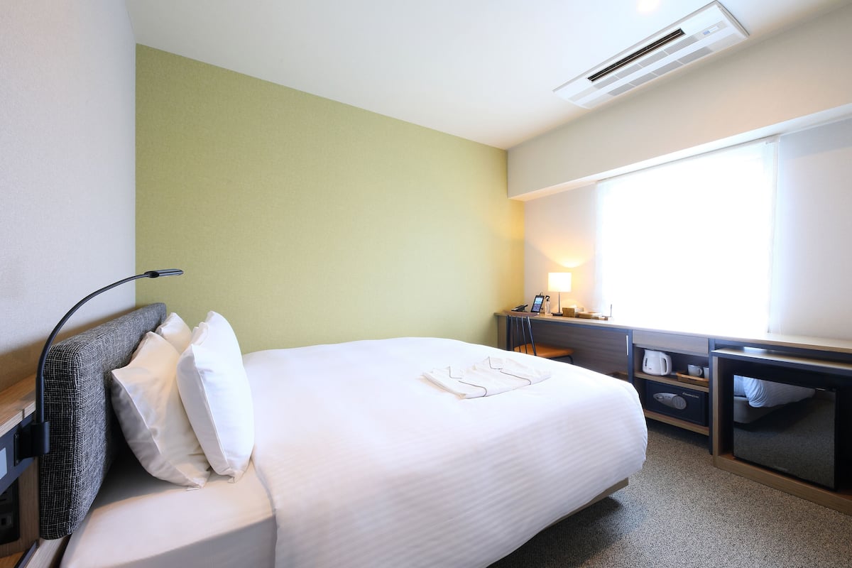 Een hotelkamer met een bed, een bureau, een stoel, een airconditioning en een raam.