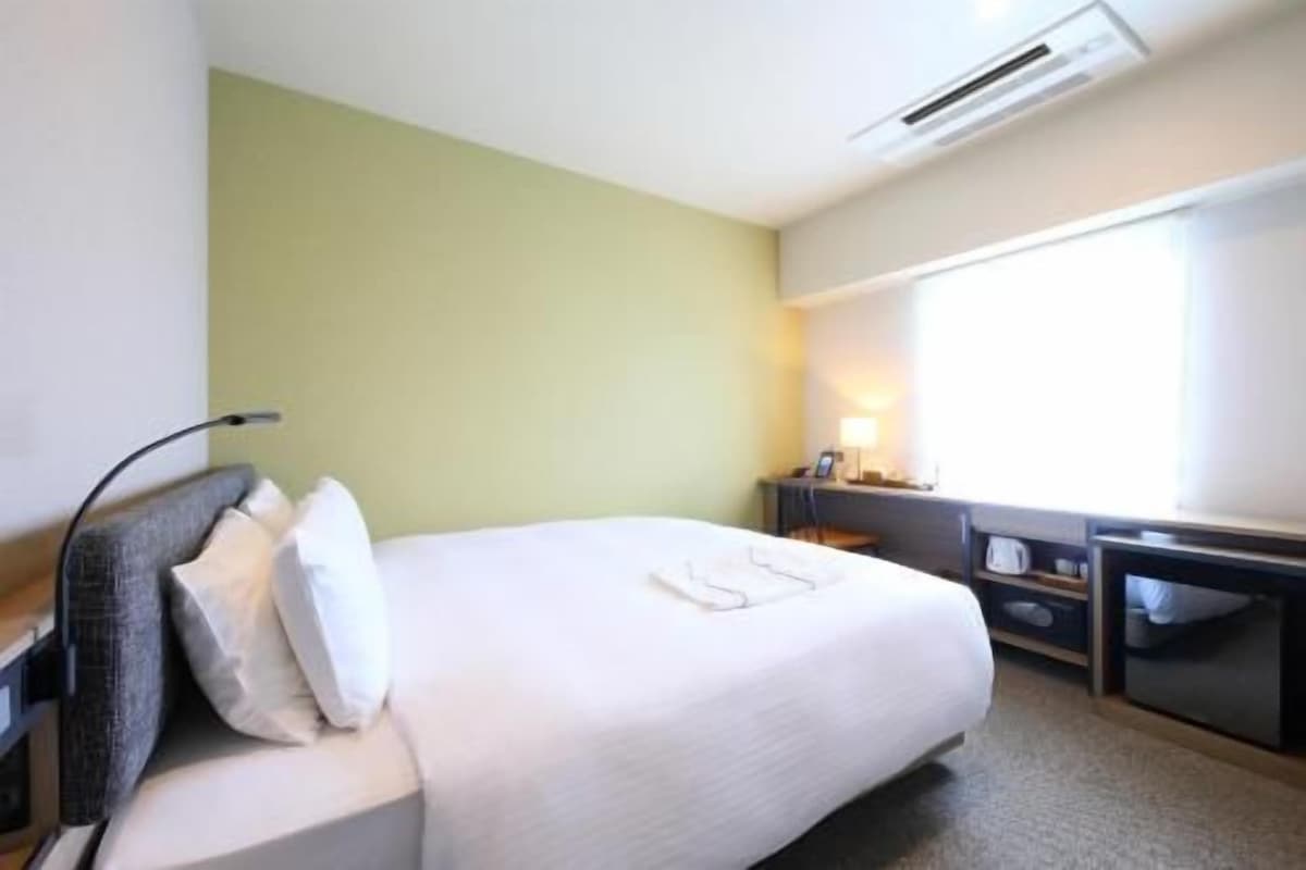 Une chambre d’hôtel avec un lit, un bureau, une chaise et une fenêtre.