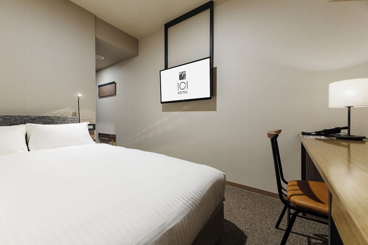 Hotelkamer met een groot bed, een bureau met stoel, een lamp en een lijst aan de muur.