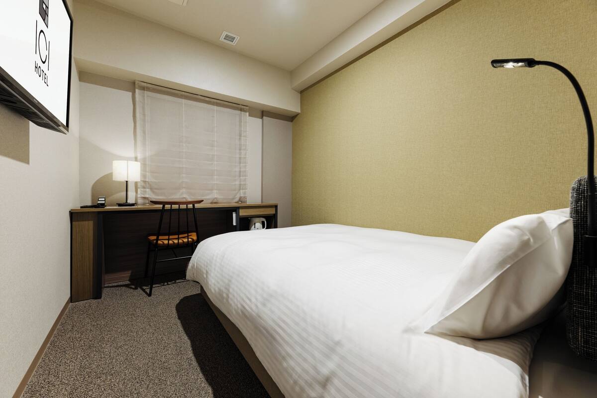 Een hotelkamer met een bed, bureau, stoel en een lamp.