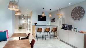 A modern kitchen with a large clock, bar stools, and a coffee machine.