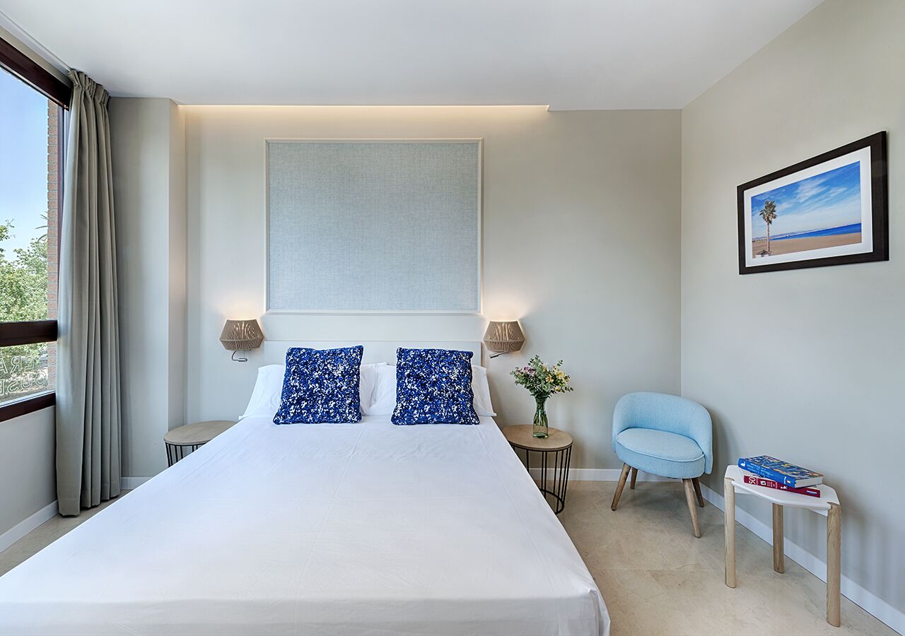 A hotel room with a large bed, two bedside lamps, a small side table, a chair, and a framed picture on the wall.