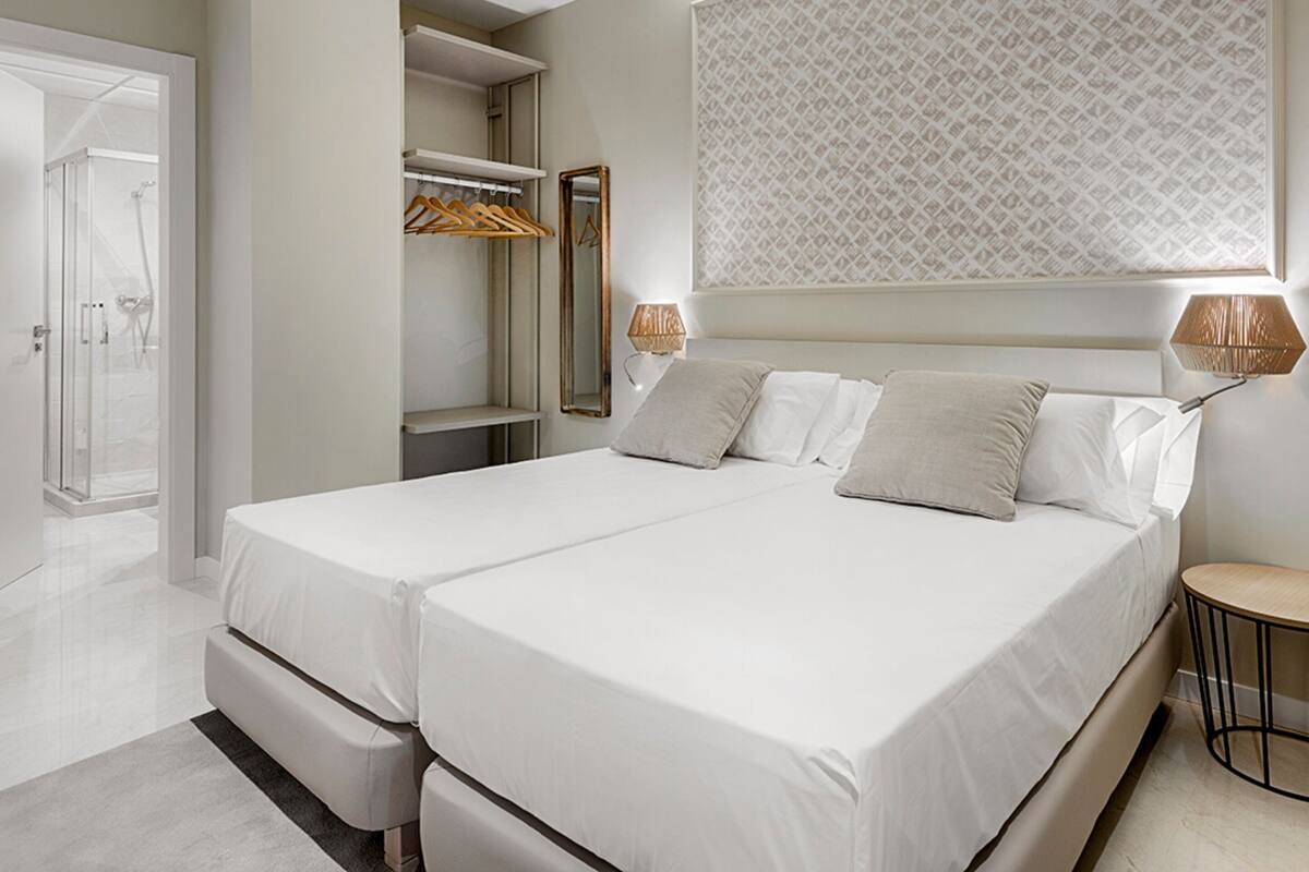 A modern bedroom with two beds, a walk-in closet, a shower, and a patterned wall.