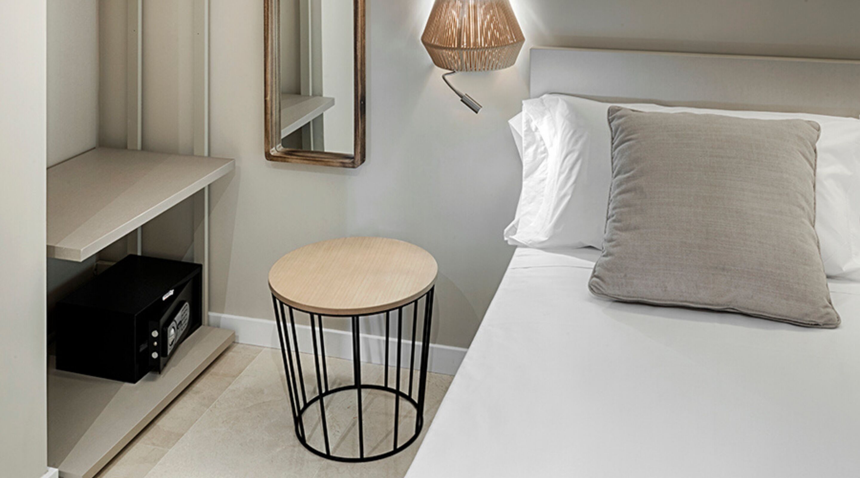 Une chambre à coucher moderne avec un lit, un tabouret rond, une table de chevet, un miroir et une lampe.