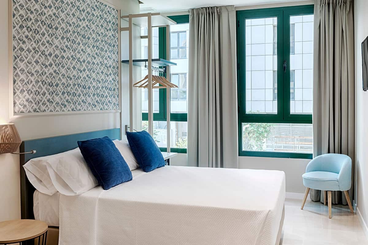 A modern hotel room with a large bed, a chair, and a window with curtains.