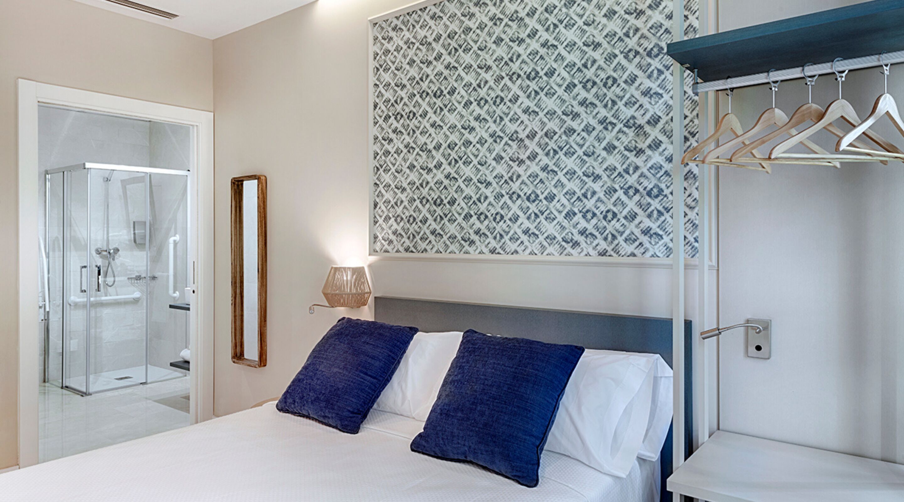 Habitación de hotel con cama, ducha, espejo, toallero de pared y pared con diseño.