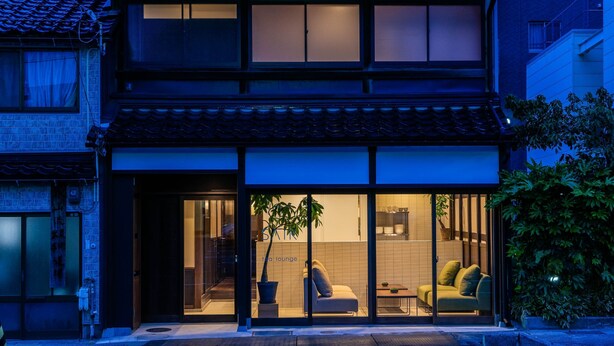 A modern two-story building with a traditional tiled roof, large sliding glass doors leading to a lounge area with a sofa and a coffee table. - Saik (Kanazawa)