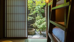 A traditional Japanese room with tatami flooring, a futon bed, a shoji screen, and a view of a garden. - Saik (Kanazawa)