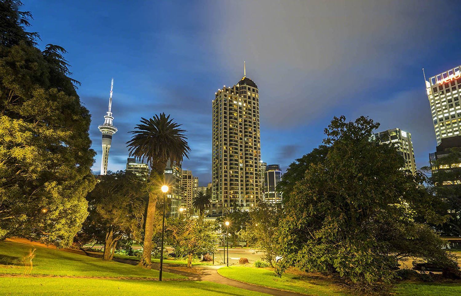 A cityscape with a prominent high-rise building, a tower, and surrounding greenery.