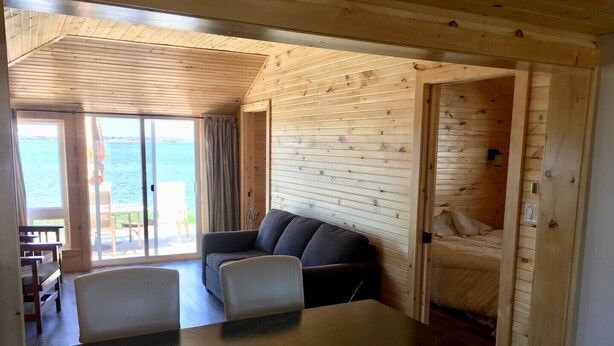 A wooden cabin interior with a dining area, a sofa, and a view of the sea.