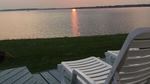 A deck with a white plastic chair facing a body of water at sunset.