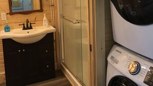A compact bathroom with a sink, mirror, and a glass-enclosed shower.