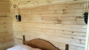 A wooden-paneled room with a single bed, a nightstand, and a wall-mounted light fixture.