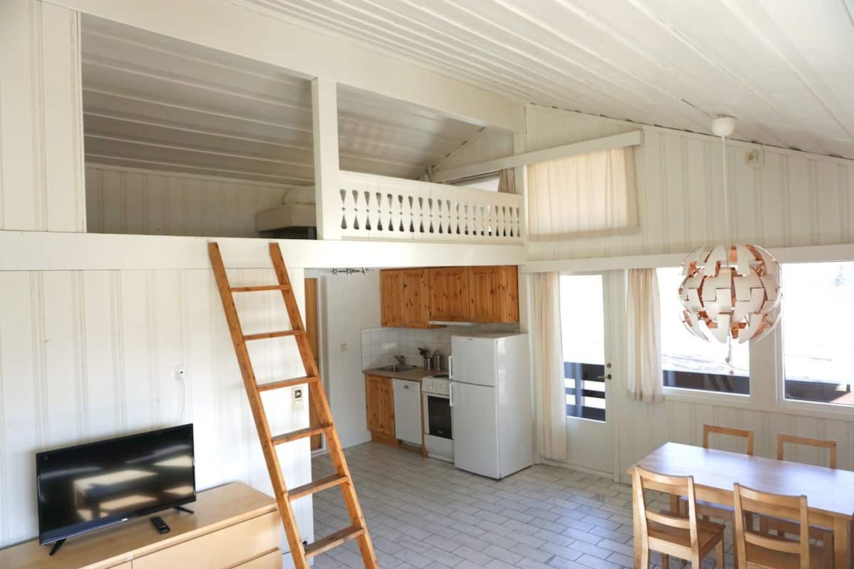Cozinha compacta com armários de madeira, geladeira e área de refeições com mesa e cadeiras.