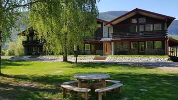 A two-story lodge with a stone facade, wooden balconies, and a dining area with picnic tables.