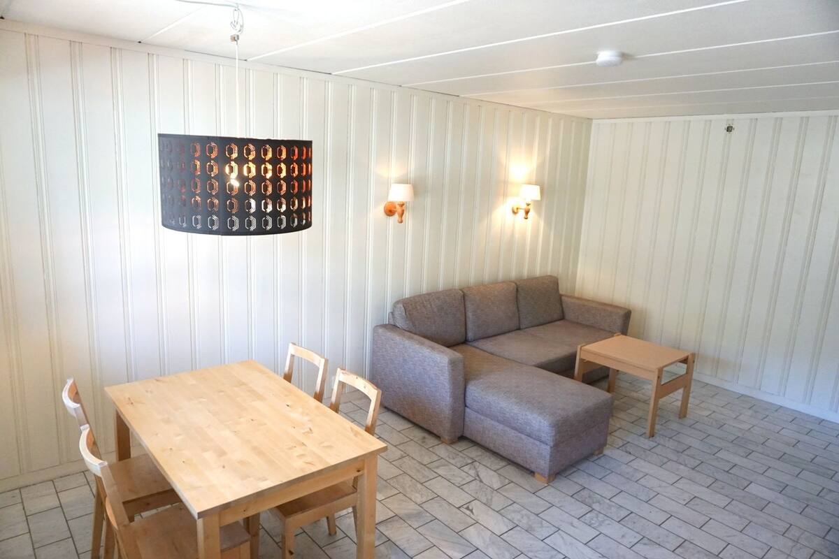 Um quarto com uma mesa de madeira, duas cadeiras, um sofá cinzento e uma pequena mesa de madeira.