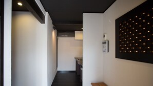 A narrow hallway with a bench, a kitchen area with a sink, and a wall-mounted light panel. - Higashiyama Aritsuki (Kanazawa)