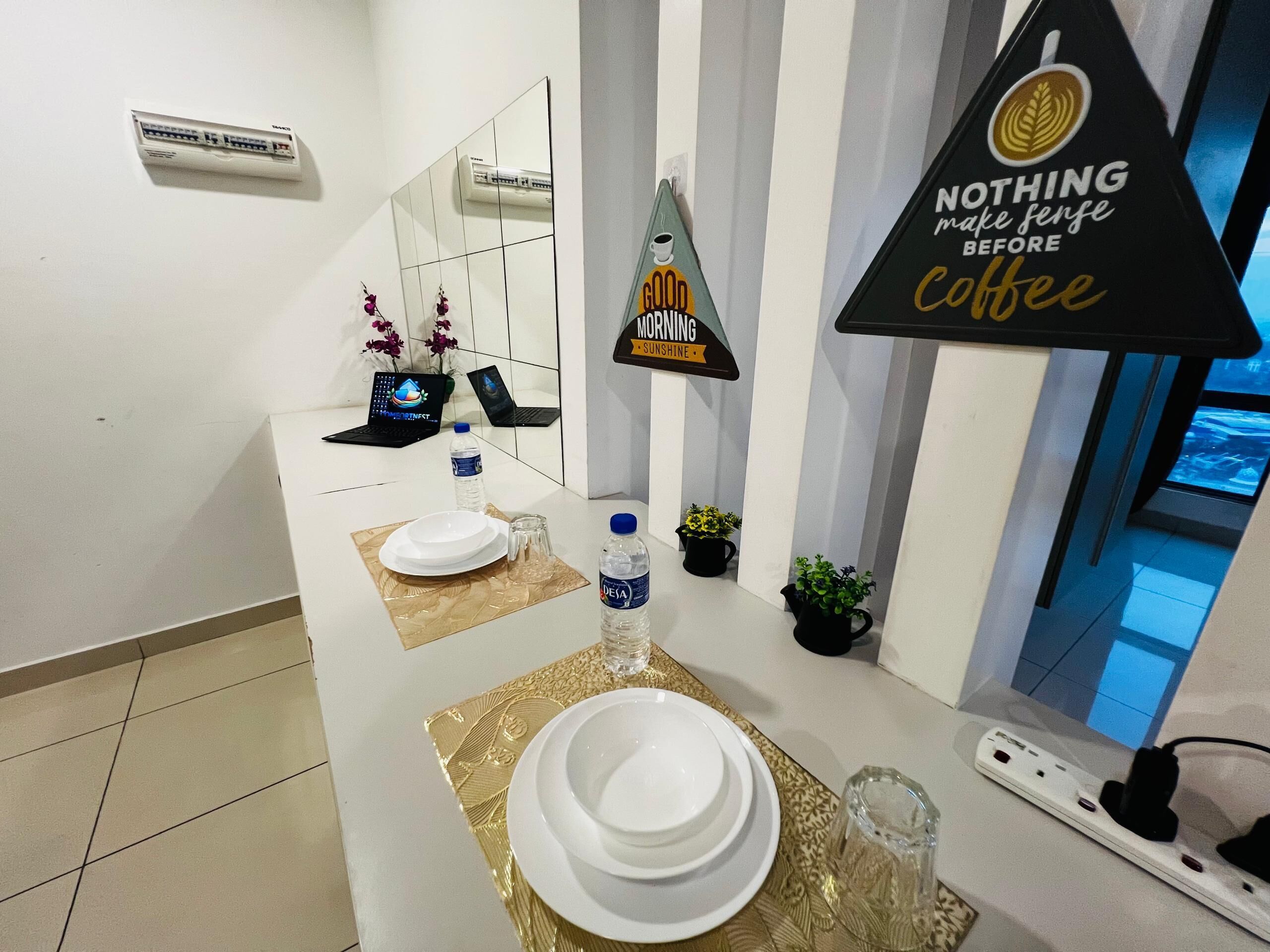 Une chambre d’hôtel au design moderne, avec un long comptoir agrémenté d’un miroir, d’une enseigne indiquant la présence d’un café et d’un ordinateur portable.