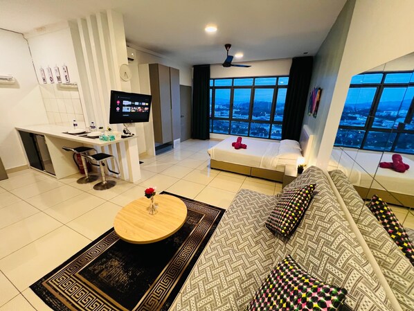 A modern hotel room with a bed, sofa, dining area, TV, and a city view.