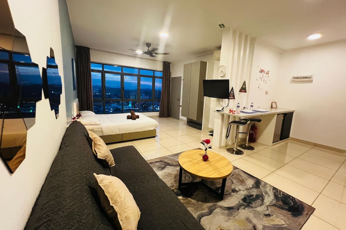 Una habitación de hotel moderna con una cama grande, un sofá, una mesita, un televisor y vistas a la ciudad.