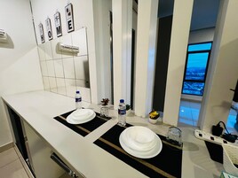 Un baño moderno con un lavamanos blanco, dos platos blancos, una botella de agua y una pequeña planta.