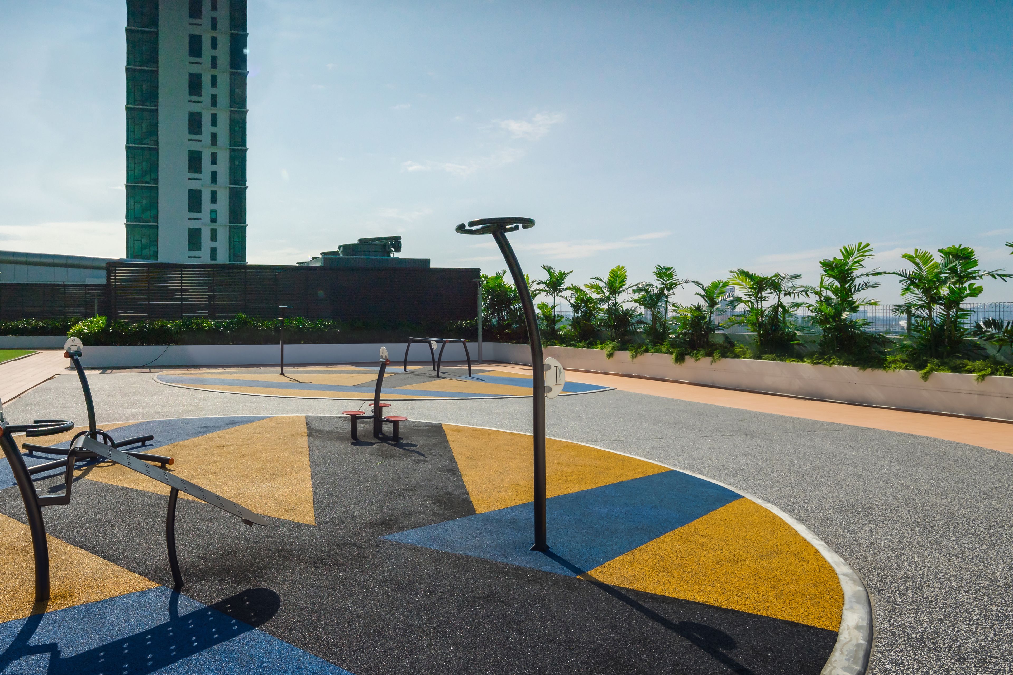 An outdoor exercise area with fitness equipment, a circular track, and a view of a tall building in the background.