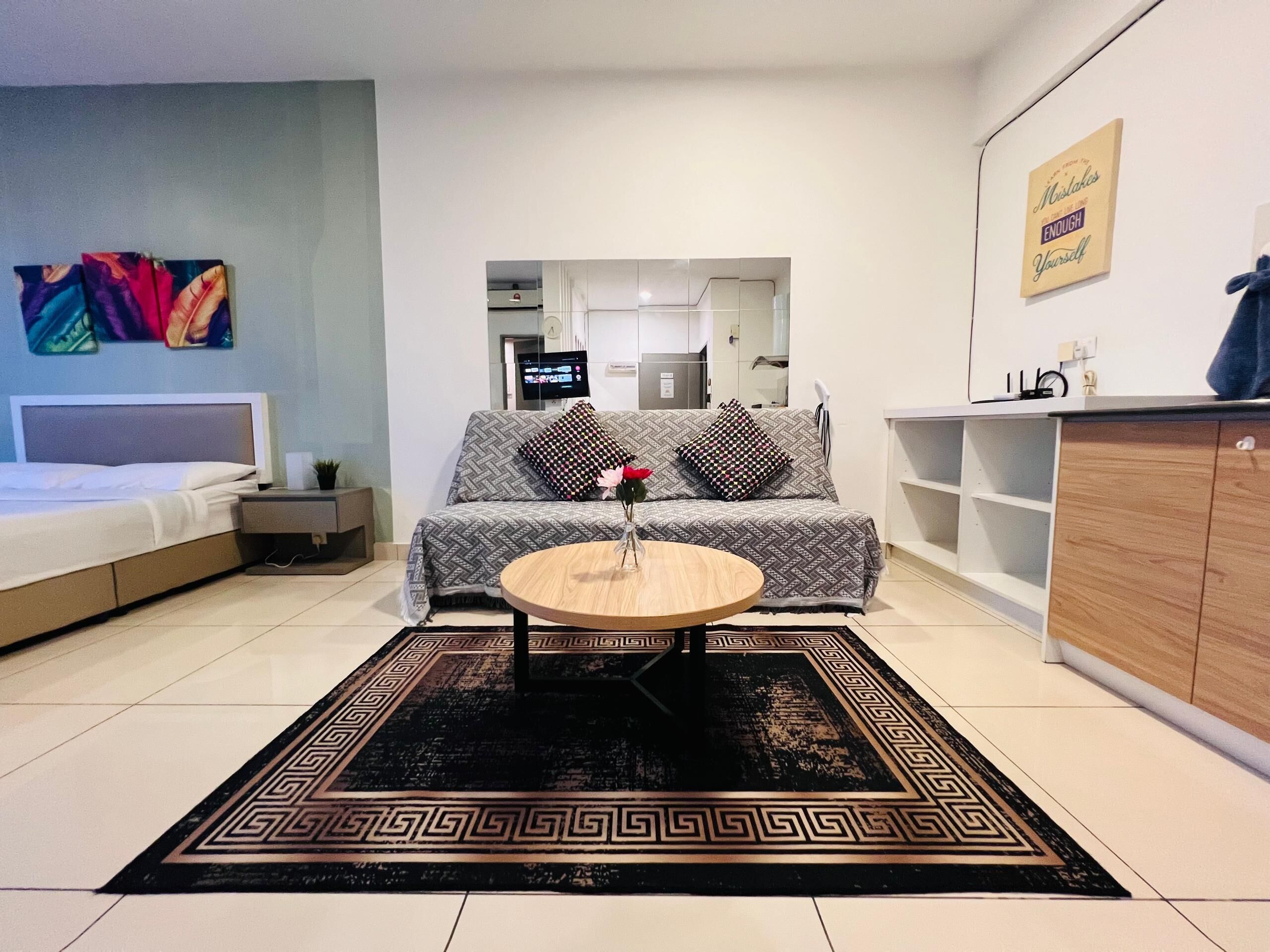 A modern living room with a sofa, a coffee table, a TV, and a kitchen area in the background.