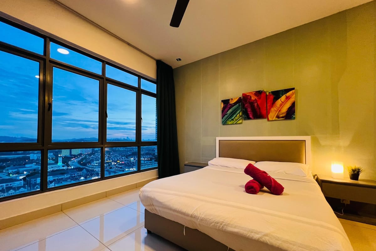 Habitación de hotel con un gran ventanal, una cama, una mesita de noche y un cuadro en la pared.