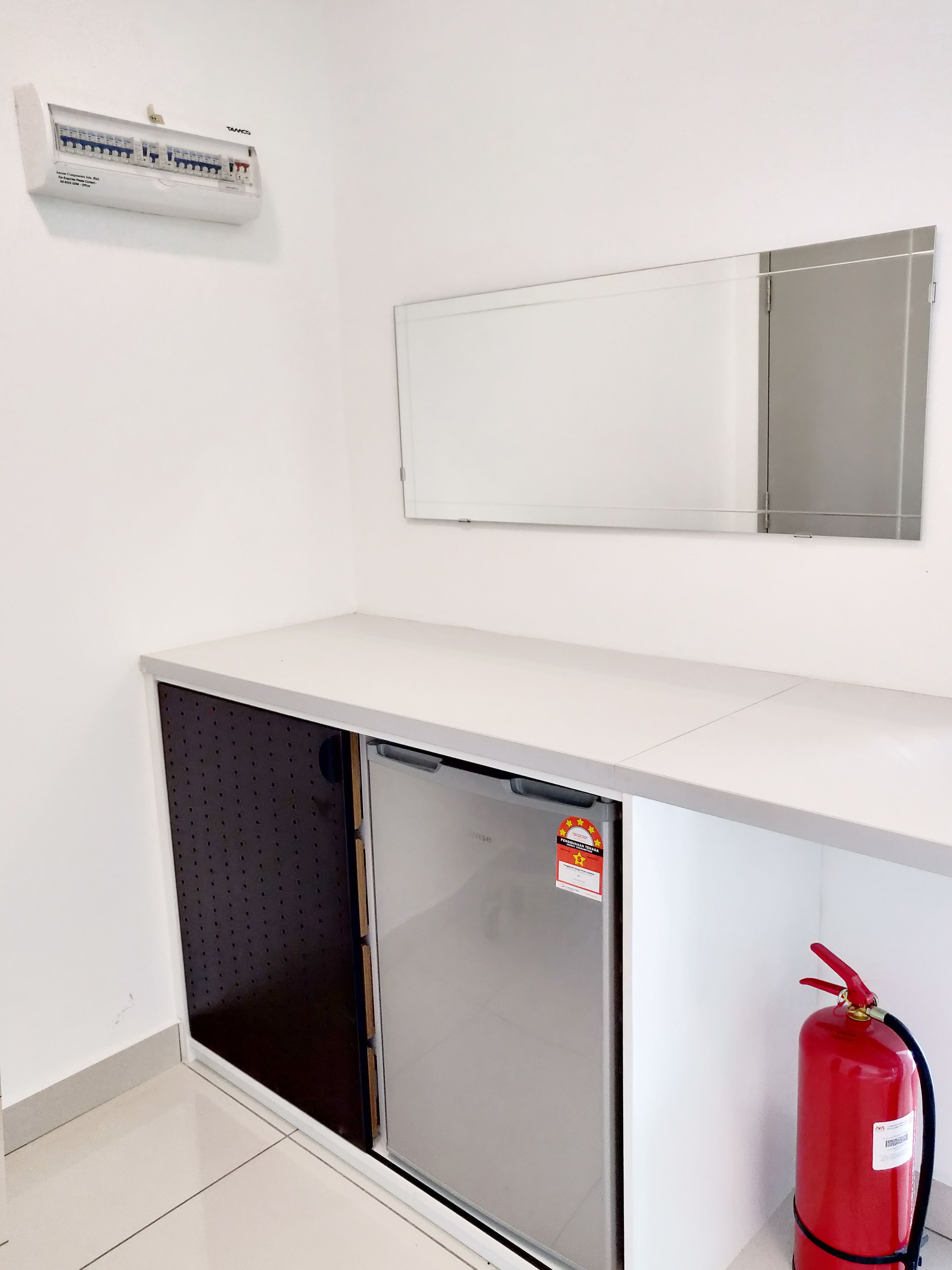 Una pequeña cocina americana equipada con refrigerador, microondas y extintor.