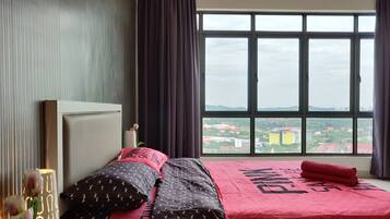 Un dormitorio con un ventanal grande, una cama con cubrecama rojo y una mesita de noche con una lámpara.