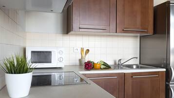 A modern kitchen with wooden cabinets, a stainless steel refrigerator, a microwave, and a sink.
