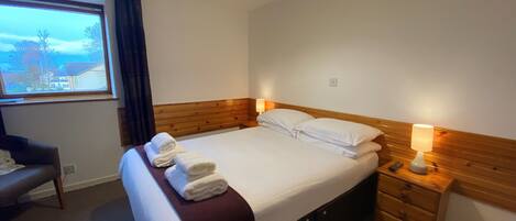 Una habitació d'hotel amb llit, taules de nit, una làmpada, una finestra amb cortines i vista a l'exterior.