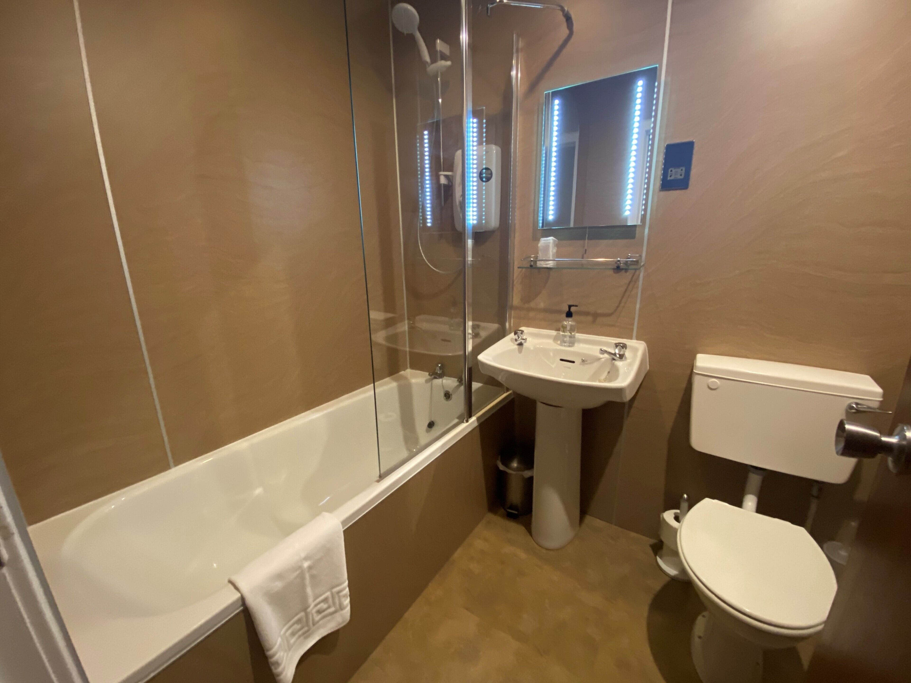 Un baño con bañera, lavamanos, inodoro y un espejo con luces LED.