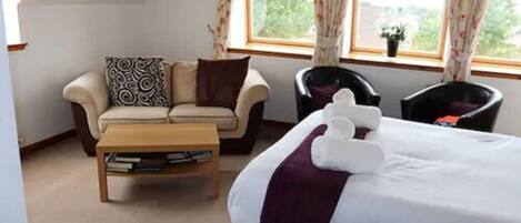 A bedroom with a bed, a sofa, two armchairs, a small table, and a window with curtains.