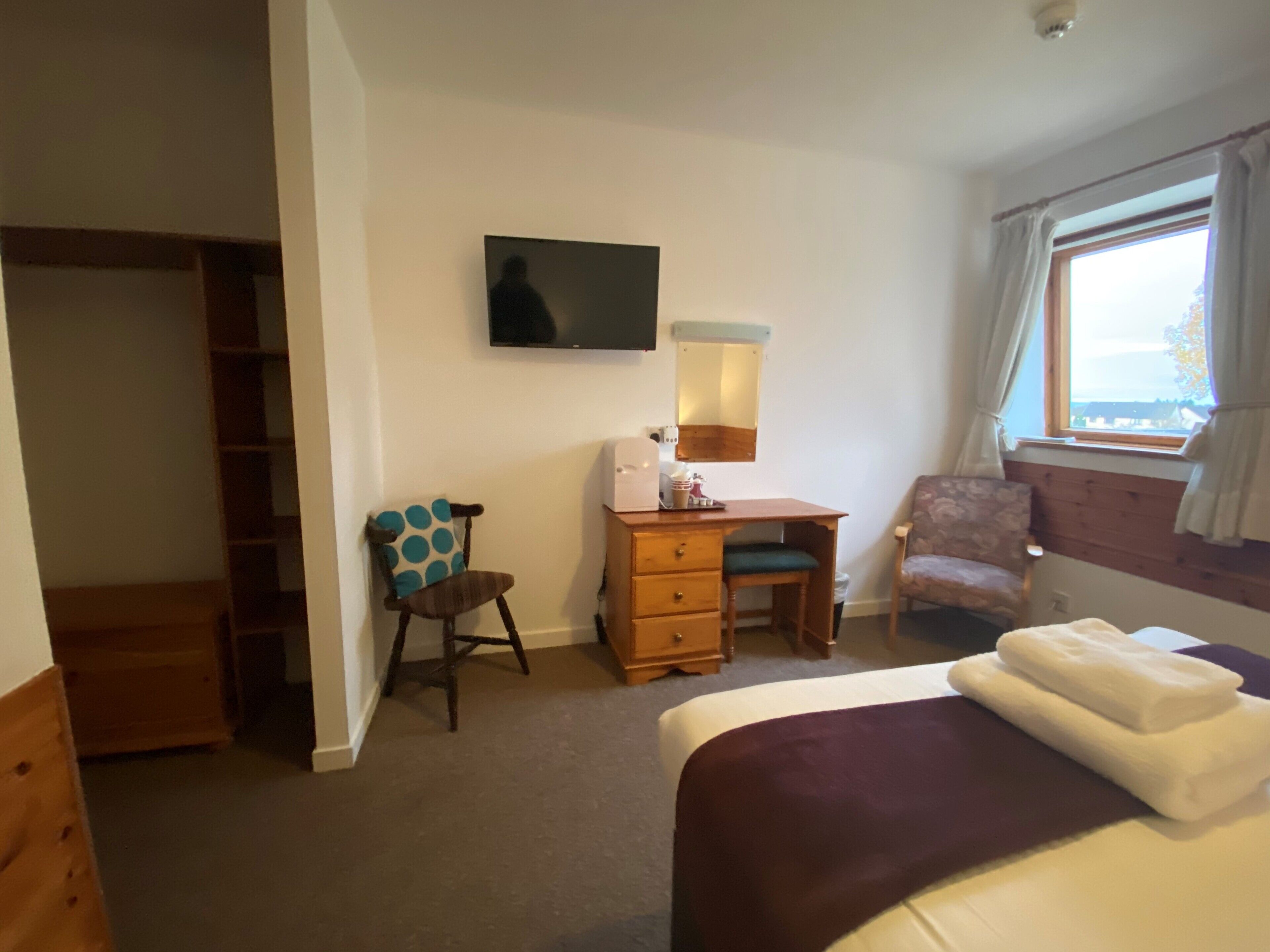 A bedroom with a bed, a desk, a chair, a television, and a window.