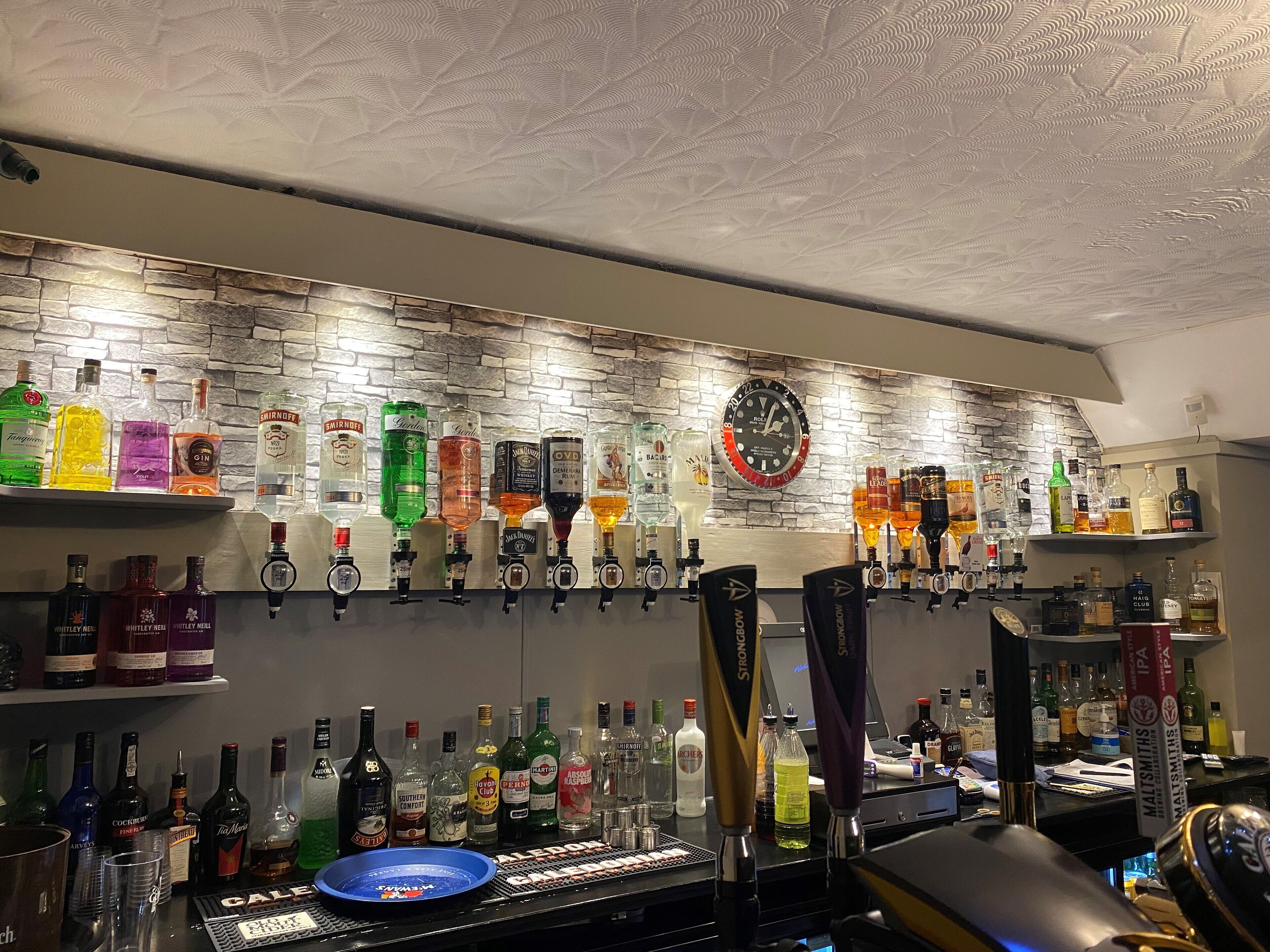 A bar area with a variety of liquor bottles and a clock on the wall.