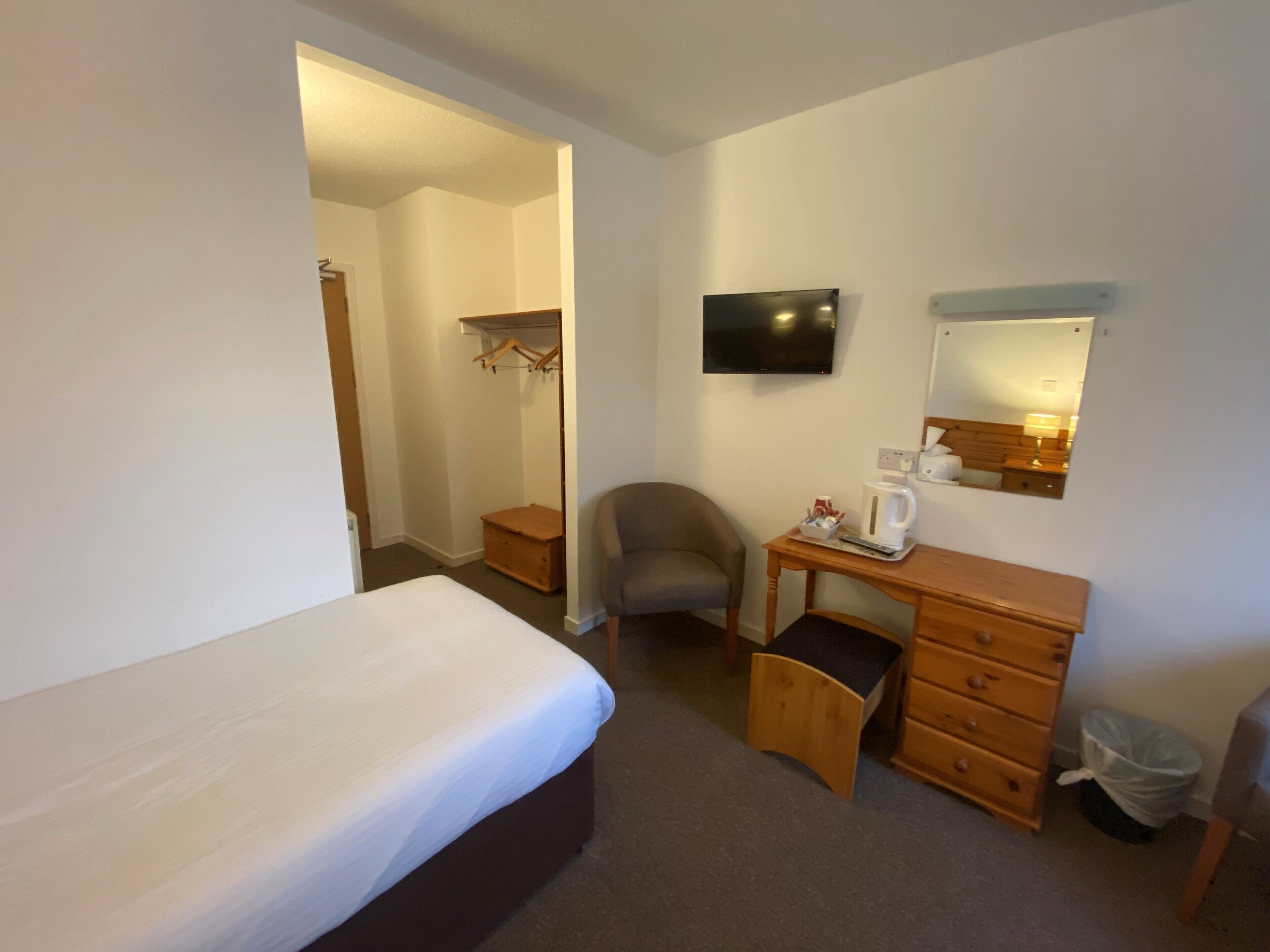 Una camera d'albergo con un letto, una scrivania con una sedia, una televisione, uno specchio e un armadio.