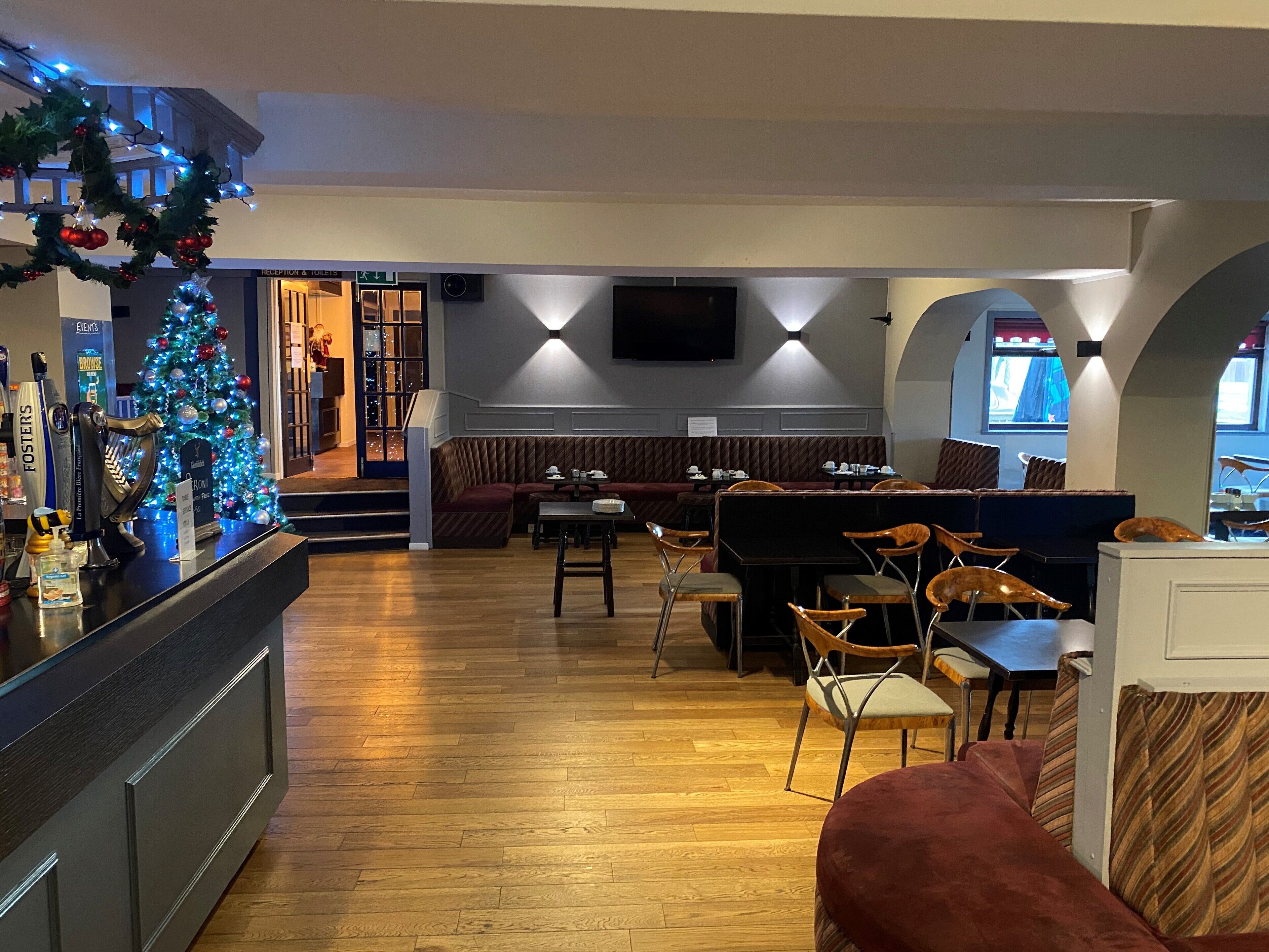 A cozy restaurant with a Christmas tree, wooden flooring, and a seating area with tables and chairs.