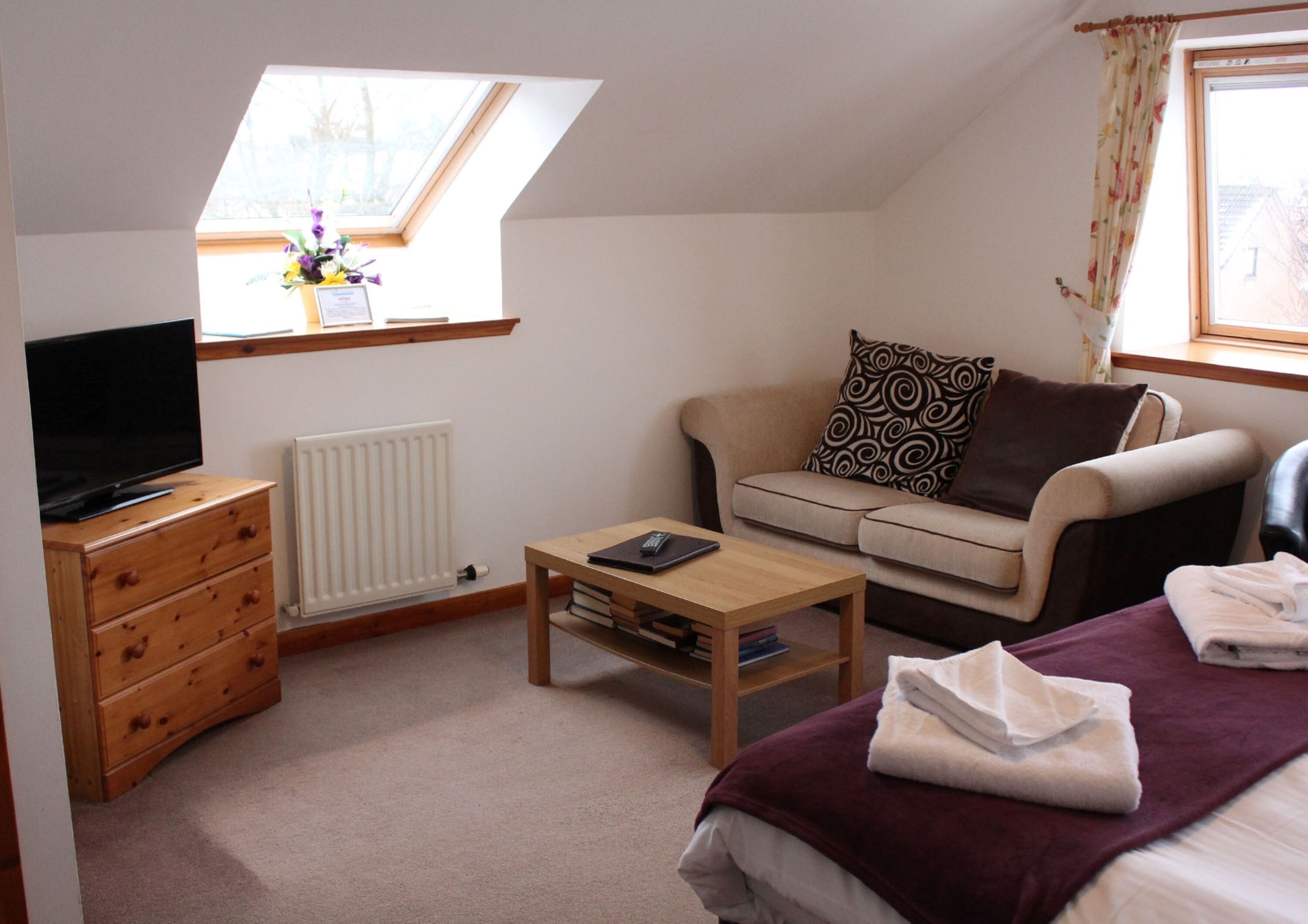 A cozy room with a sofa, a coffee table, a TV on a dresser, and a bed with a blanket.