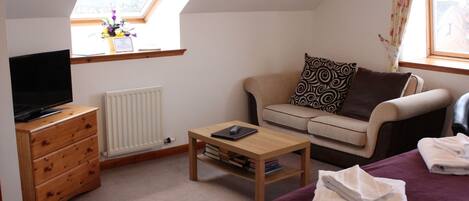 A cozy room with a sofa, a coffee table, a TV on a dresser, and a bed with a blanket.