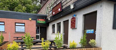 A building with signs for 'Mario's Last Chance Saloon' and 'Mario's Bar' offering live sports, pool, darts, and a free house.
