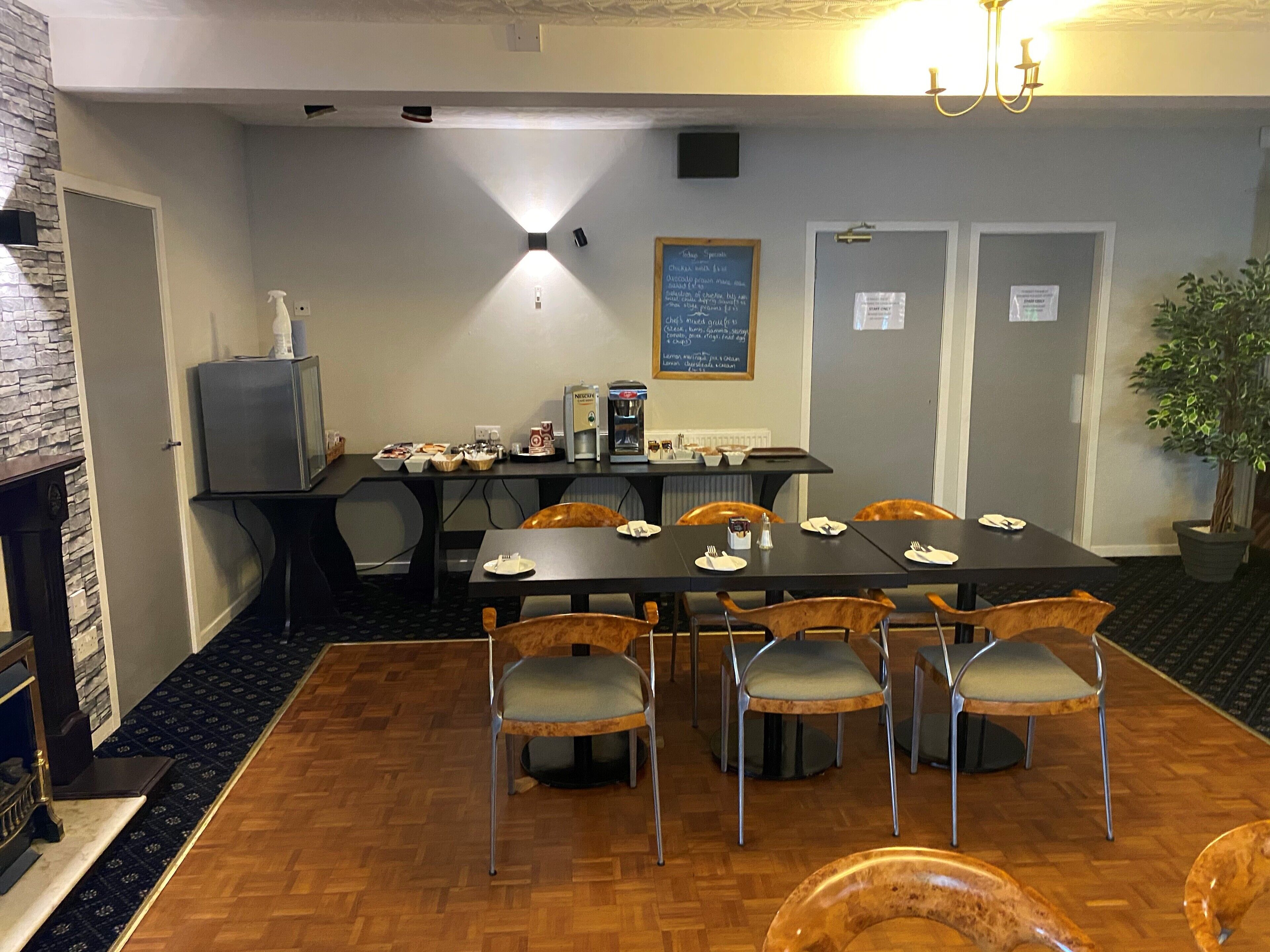 A dining area with a long table, chairs, a coffee machine, and a chalkboard menu.