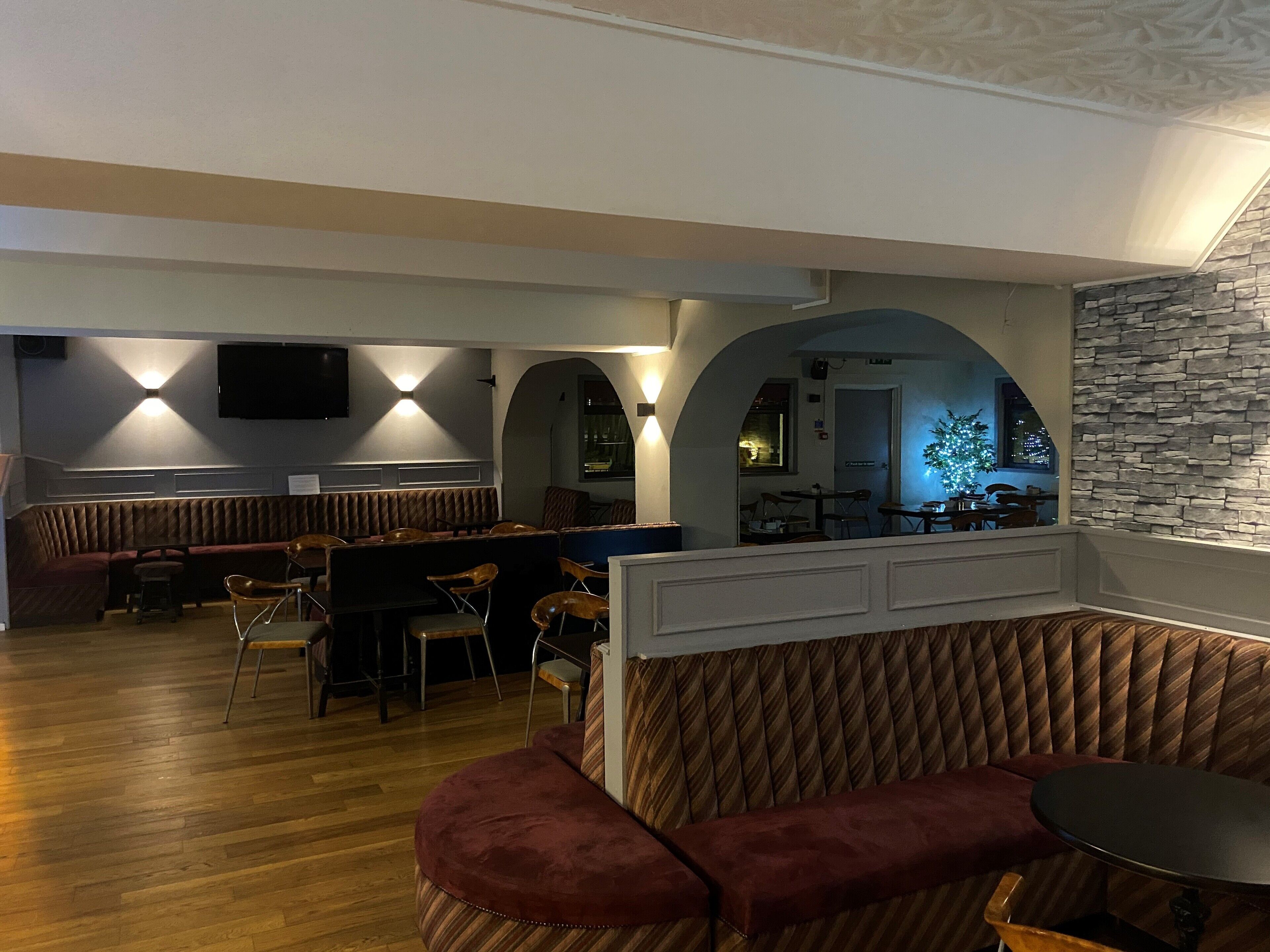 A cozy restaurant with wooden flooring, cushioned seating, and a stone accent wall.