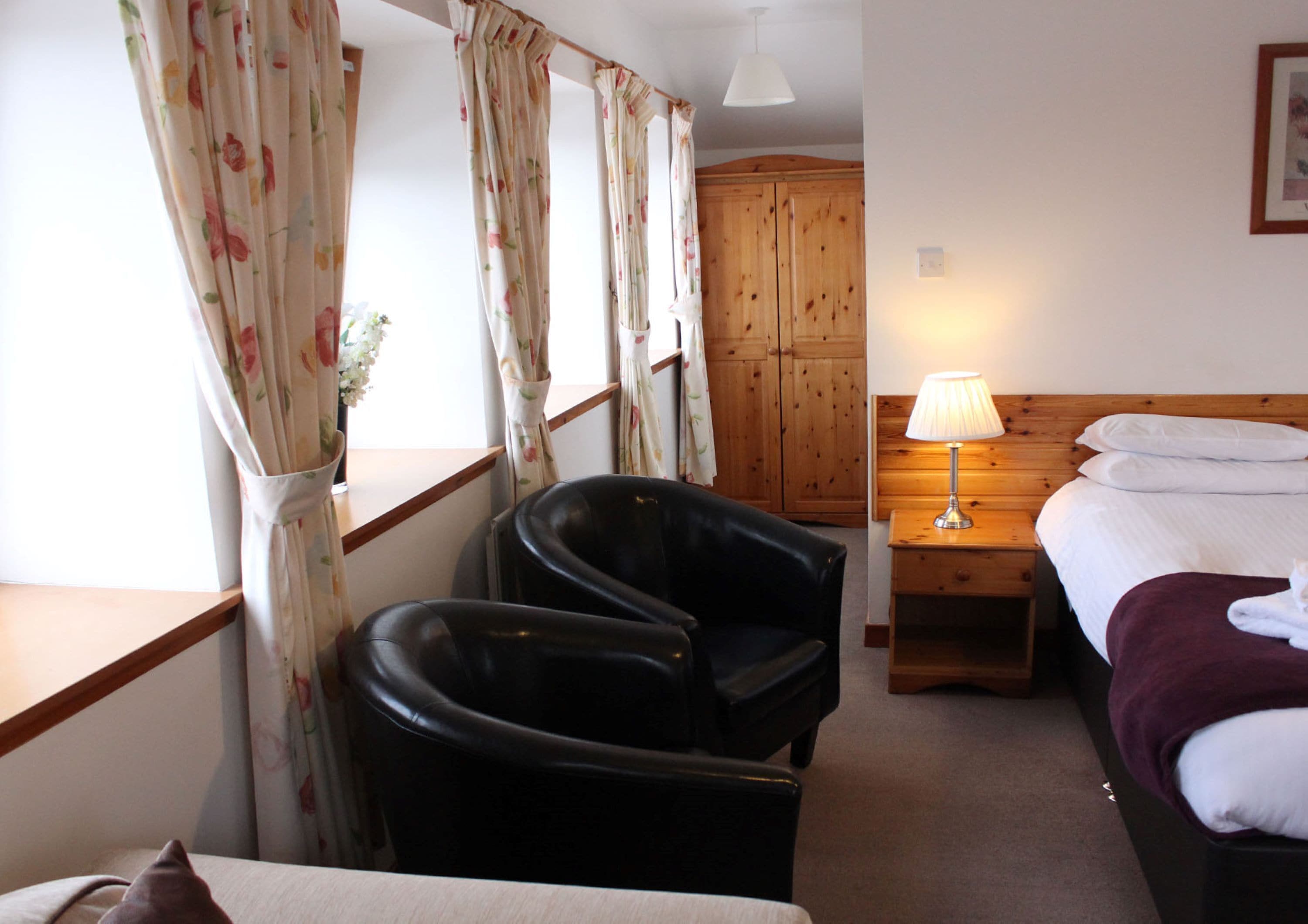 A hotel room with a bed, a desk, a chair, a wooden wardrobe, and a lamp.