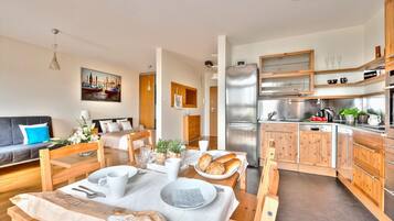 A modern kitchen with wooden cabinets, a stainless steel refrigerator, and a dining area with a table set for two.